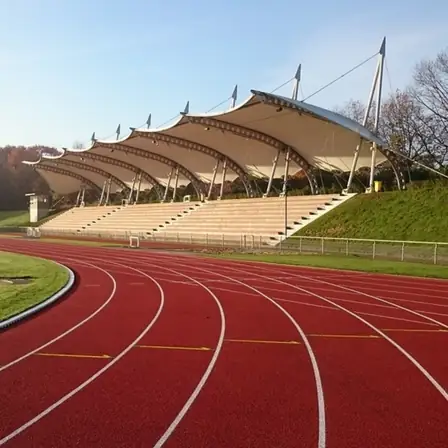An empty outdoor athletics track in morning light, red lanes curving past a covered grandstand.